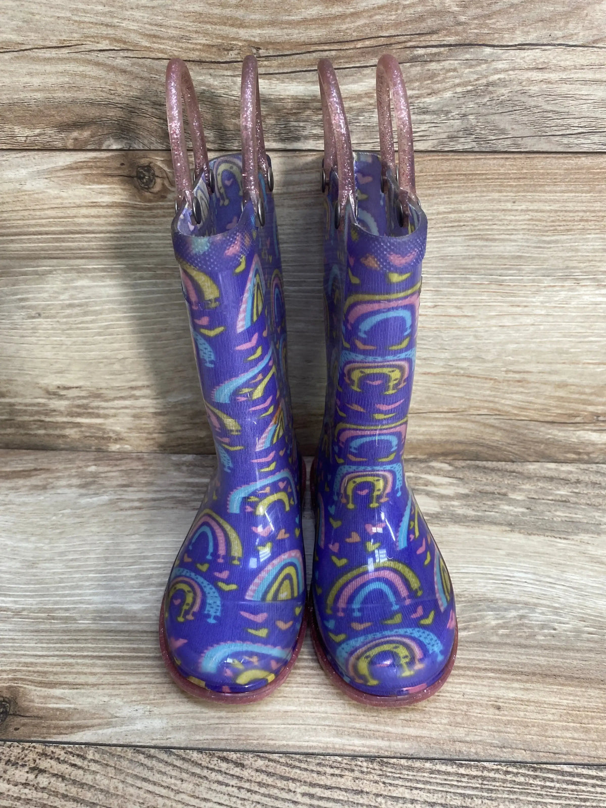 Colorful children’s rain boots with rainbow patterns and glitter handles on wood floor