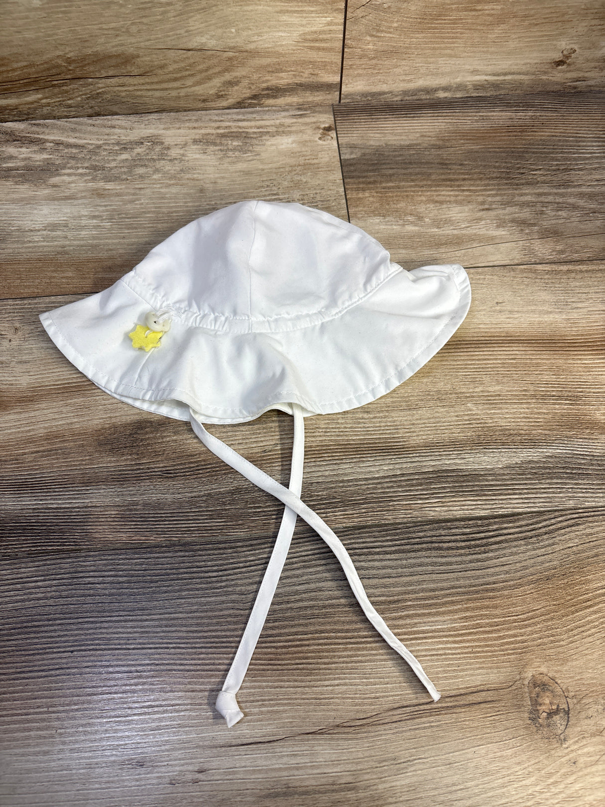 Top-down view of iPlay swim bucket hat in white showing wide brim, chin ties, and yellow star button on wood background