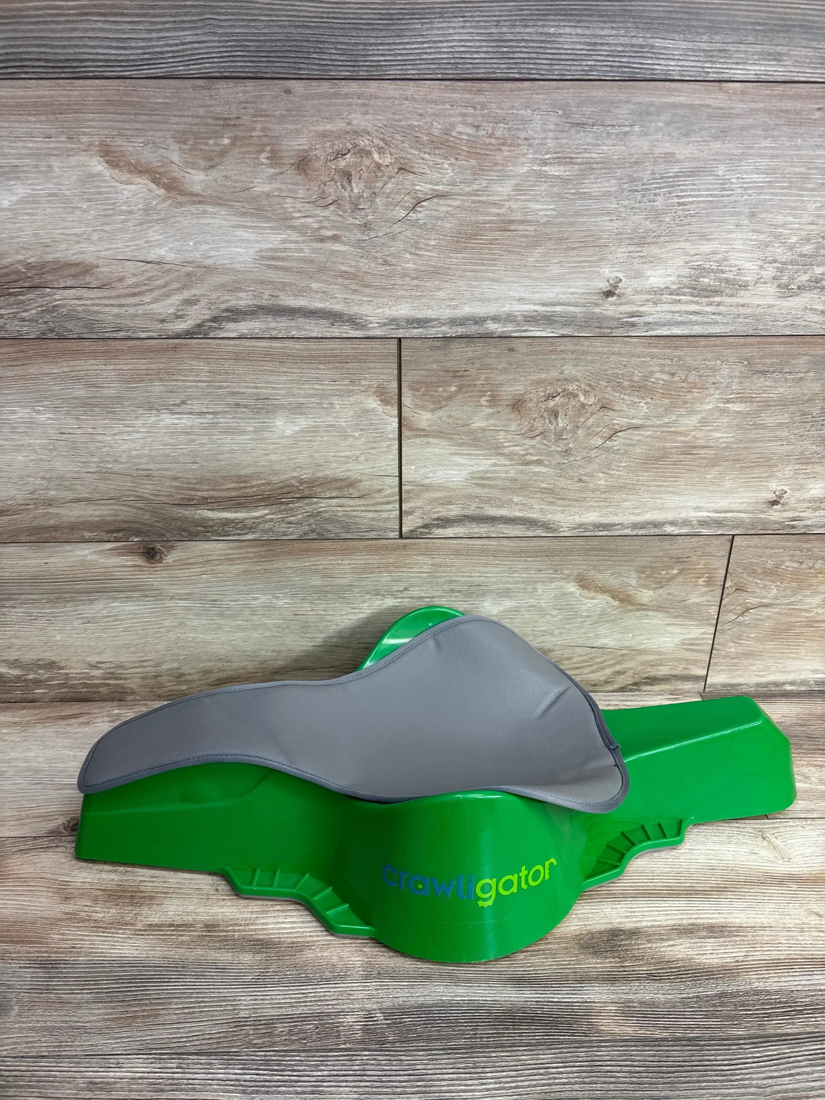 Green Crawligator baby crawling aid with grey padded seat on wooden floor