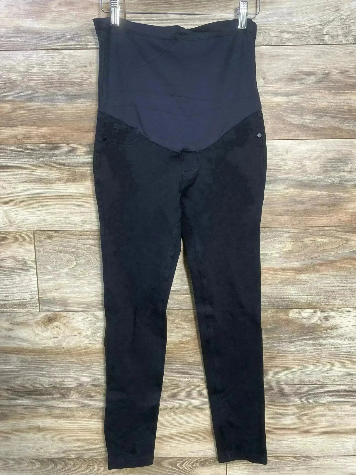 Front view of Pink Blush maternity full-panel black pants showing high-stretch belly panel and slim leg, hung on wood floor background