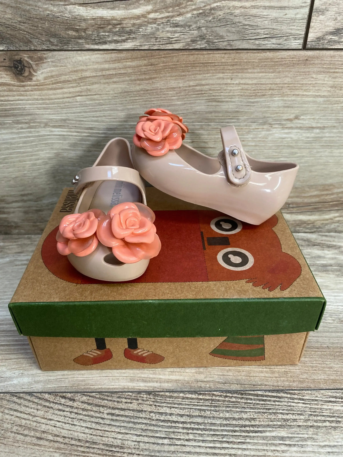 Angled view of Mini Melissa Ultragirl girl's beige-pink flats with coral flower appliques and Mary Jane strap on shoe box