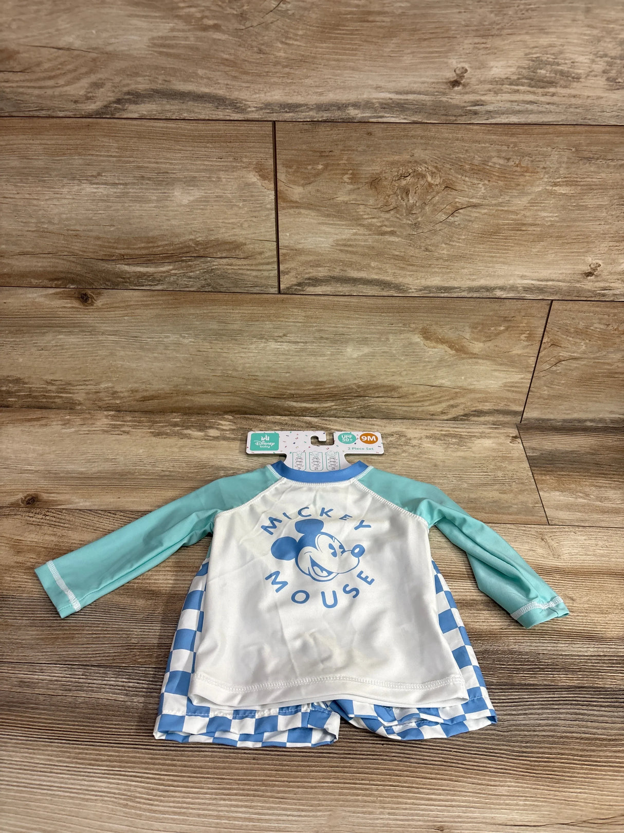 Flat lay of Mickey Mouse rash guard set with white top, blue Mickey print and mint sleeves, blue-and-white shorts, size 9M