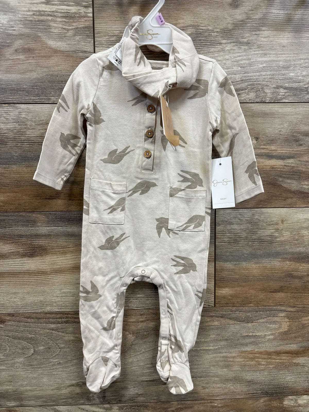 Beige baby romper with bird print, wooden buttons, and matching scarf on wood background