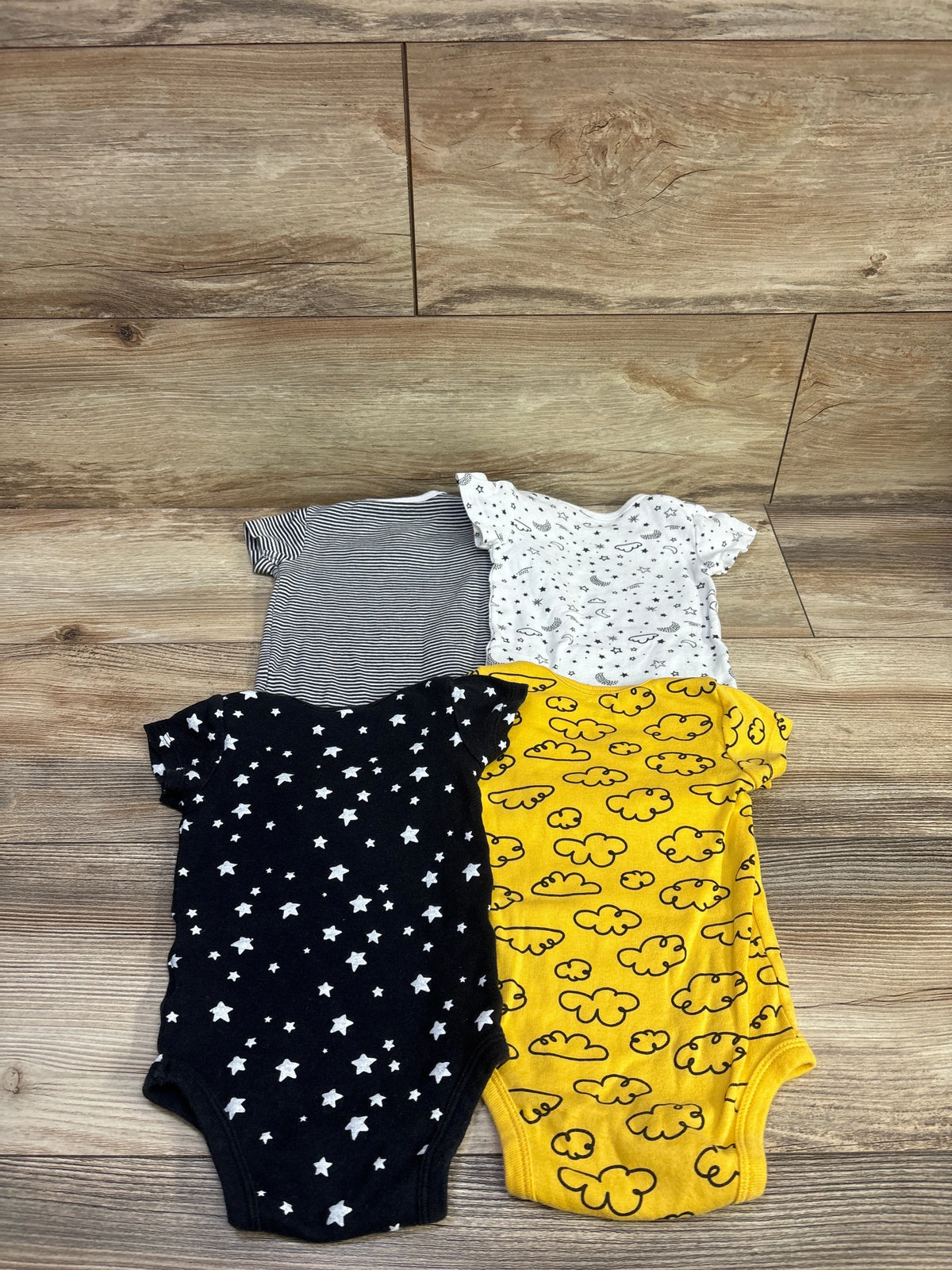 Overhead view of four Gerber baby bodysuits in striped, printed, star, and cloud patterns on a wood floor