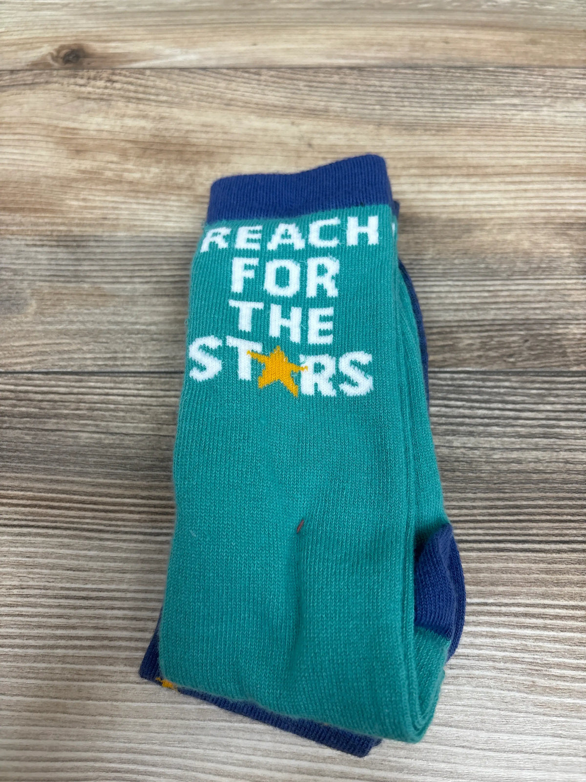 Front view of Cat & Jack knee-high socks showcasing teal fabric, navy trim, and Reach for the Stars text on a wood background