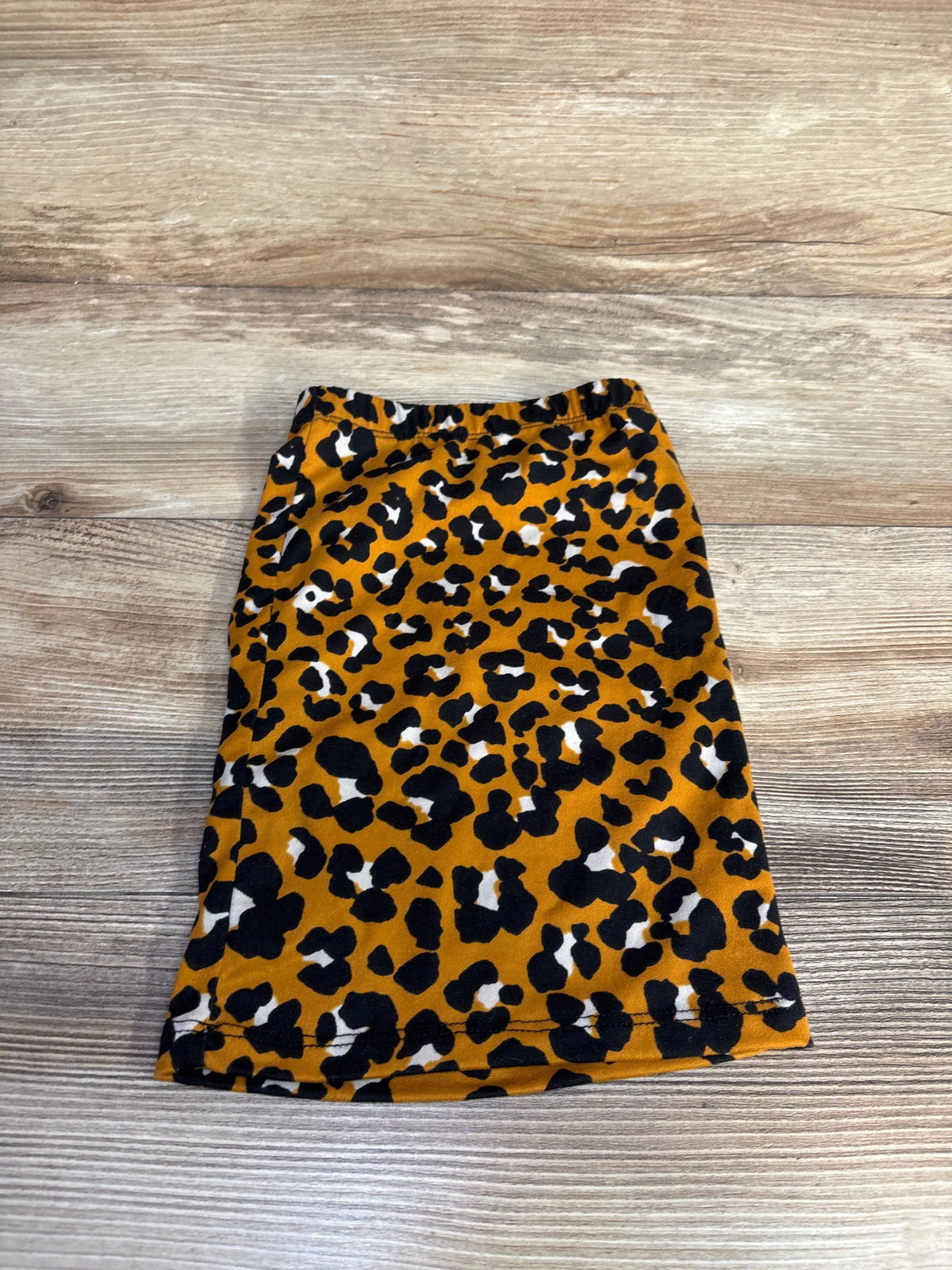 Front view of Little Loper leopard print skirt in brown, showcasing elastic waistband on a wood background