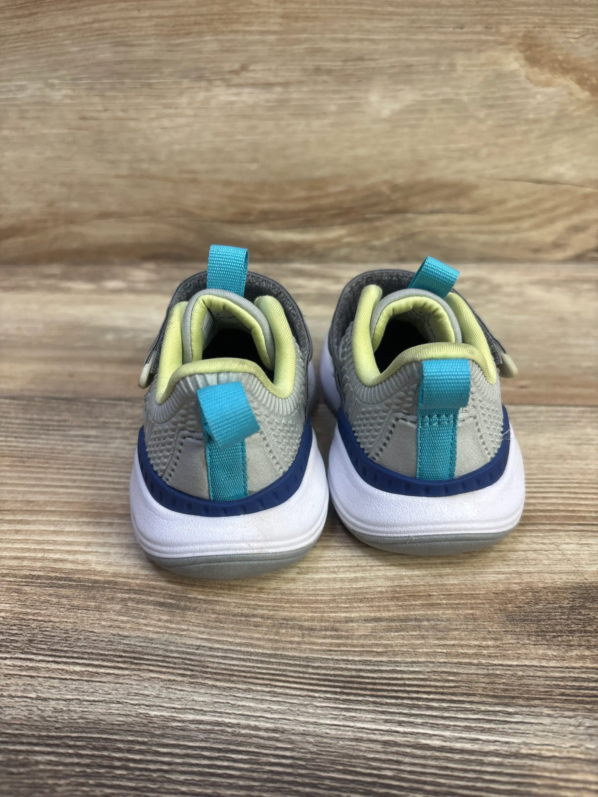 Rear view of All In Motion Peyton sneakers in grey with turquoise heel pull tabs, yellow lining and white cushioned soles on wood background