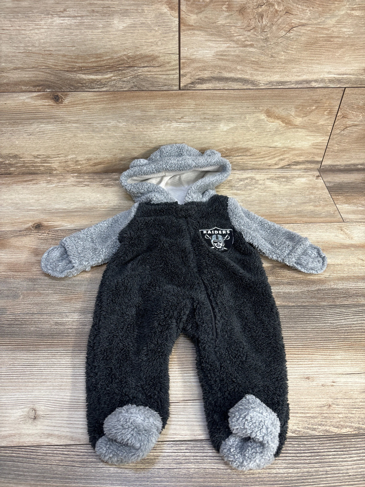 Black and gray Raiders baby fleece onesie with hood and team logo on wood floor