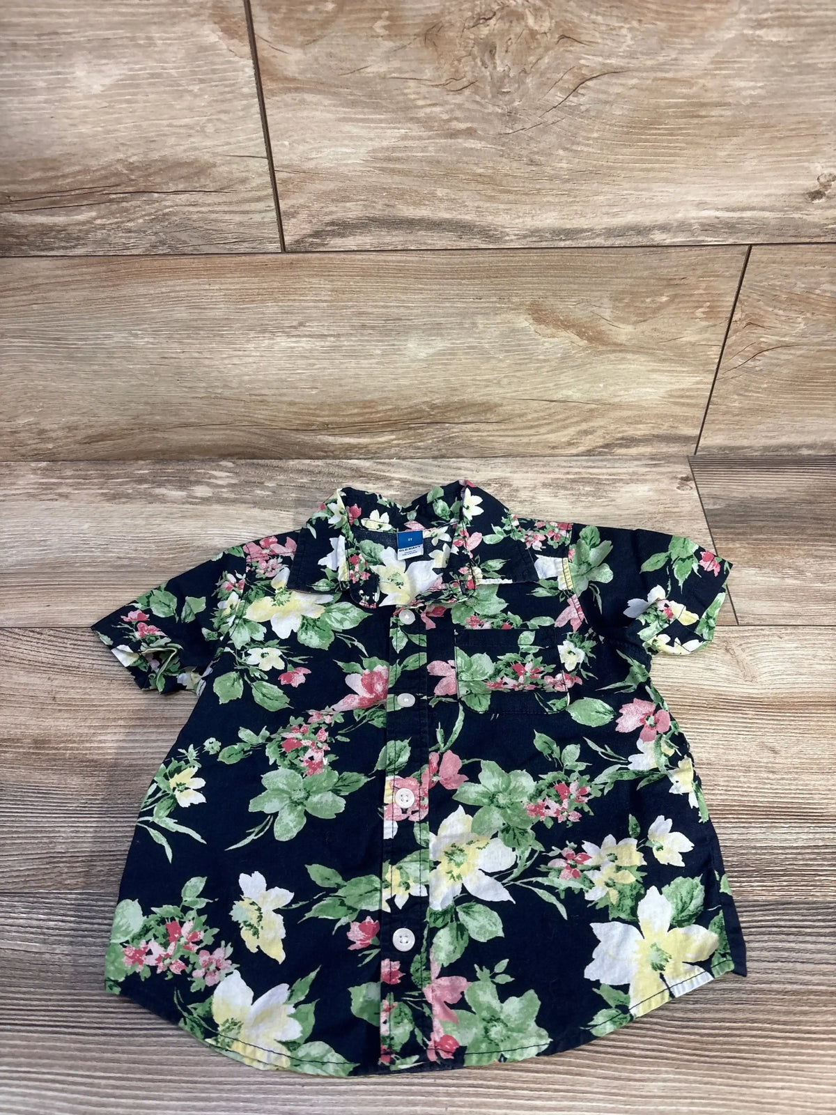 Flat lay of toddler navy Old Navy short-sleeve button-up shirt showcasing floral print and front pocket on wood floor