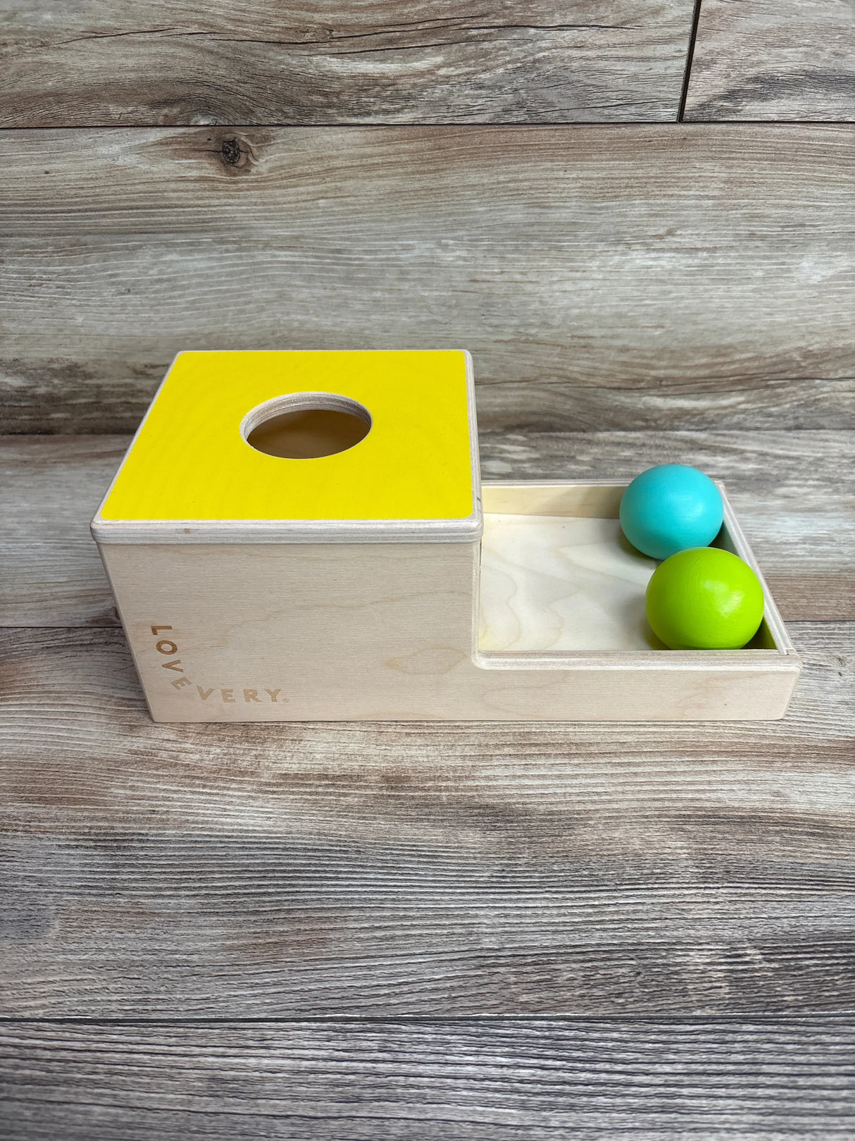 Lovevery wooden toddler ball drop toy with yellow top and blue and green balls on wooden floor