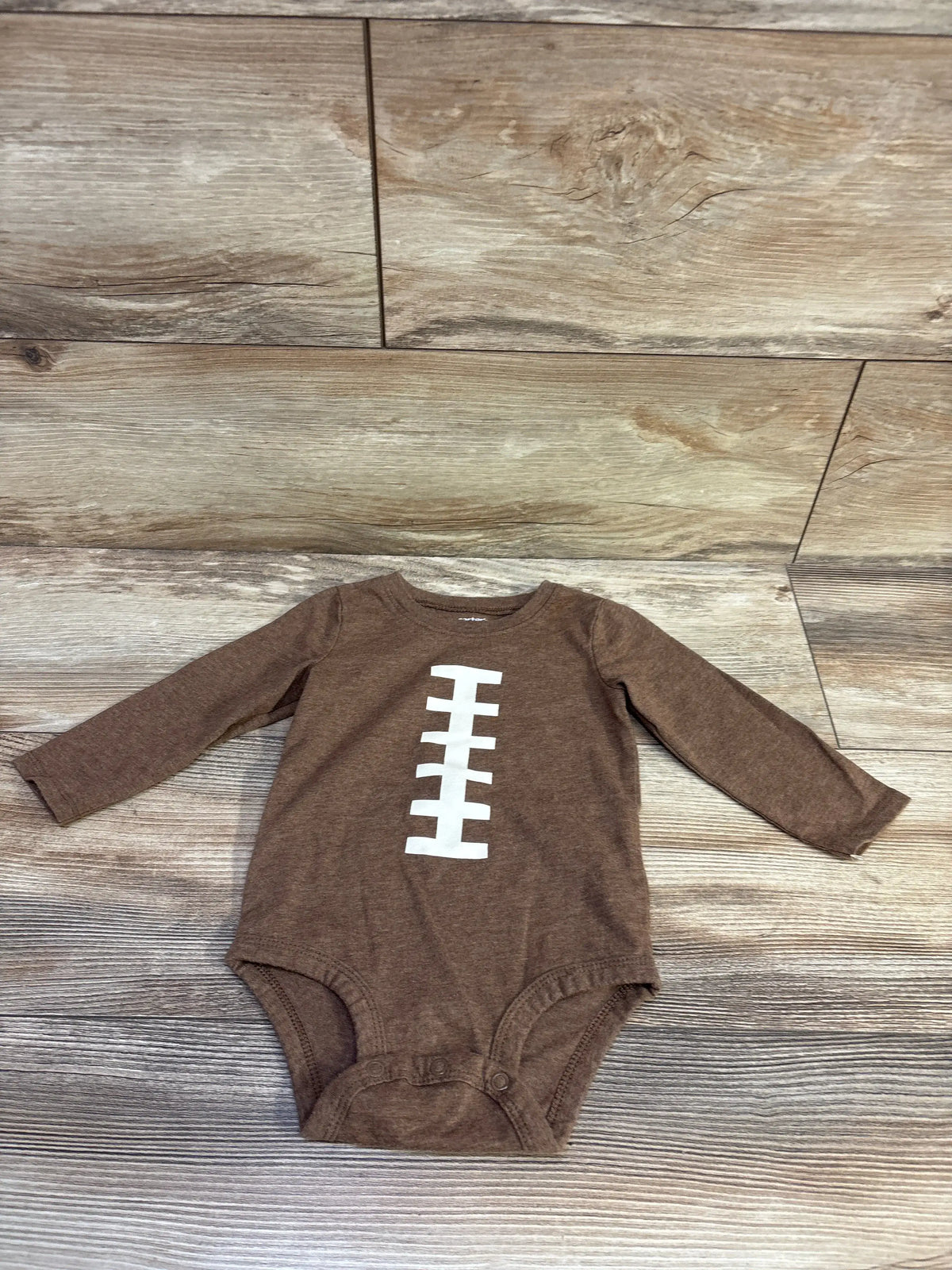 Brown long sleeve Carter's baby football bodysuit with white laces graphic on wood background