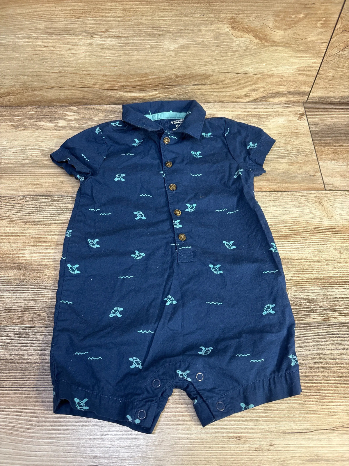 Front view of Child Of Mine navy polo romper for 6–9 months, showcasing turtle print and button placket on a wood floor