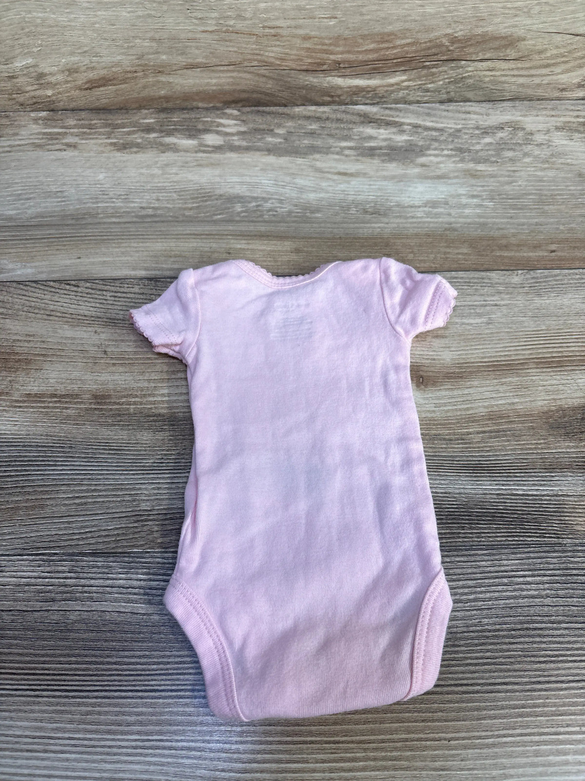 Front view of Simple Joys pink preemie bodysuit showcasing short sleeves and leg openings on a gray wood background