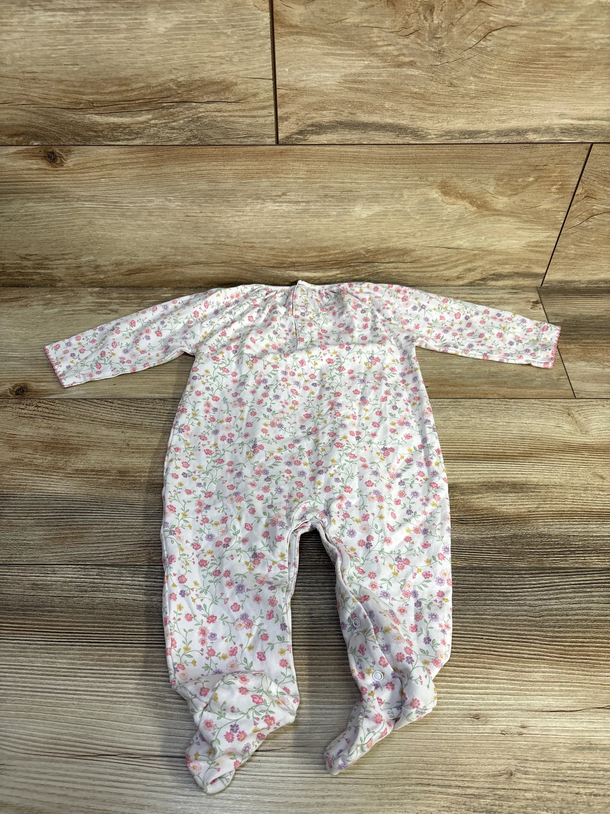 Top view of Kissy Kissy white floral footed coverall showcasing long sleeves and footed legs on a wood floor