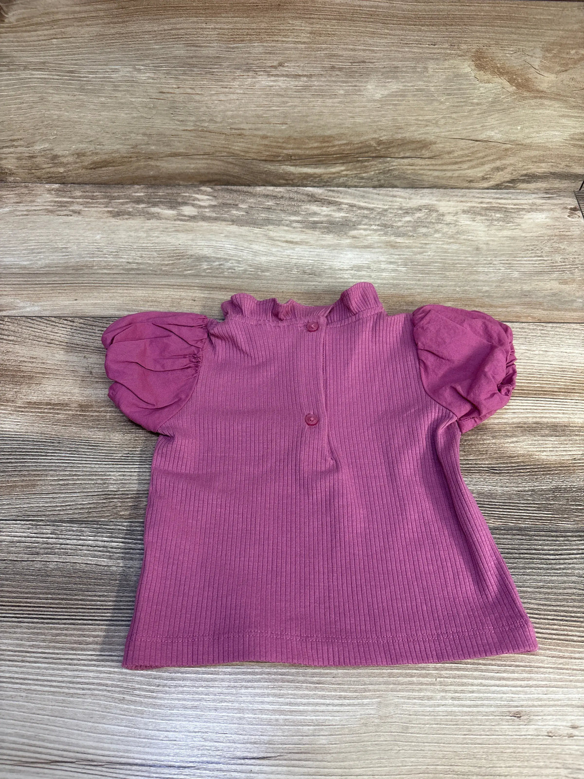 Top-down view of Janie & Jack mauve ribbed collared puff sleeve top with button front on wood-grain background