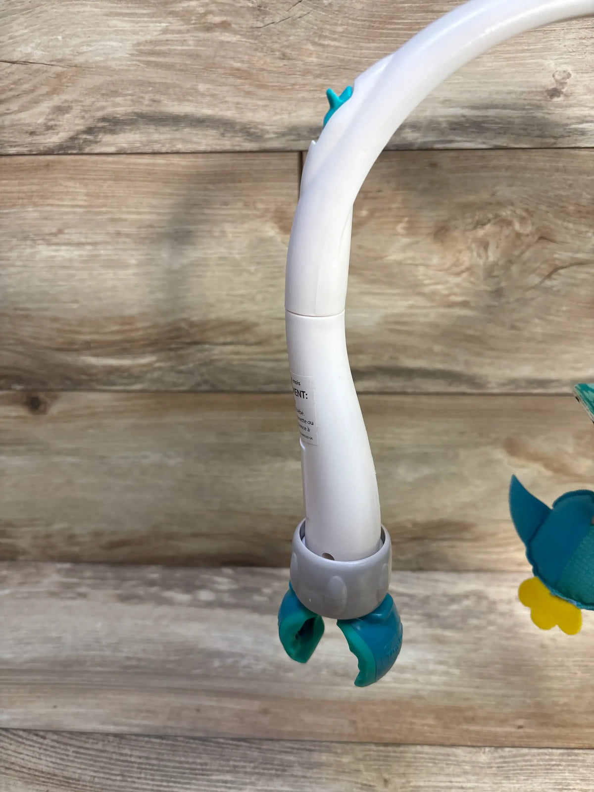 Side view of Tiny Love 3-in-1 Take Along Mobile, Meadow Days showcasing white curved arm and teal attachment base on wood-grain background