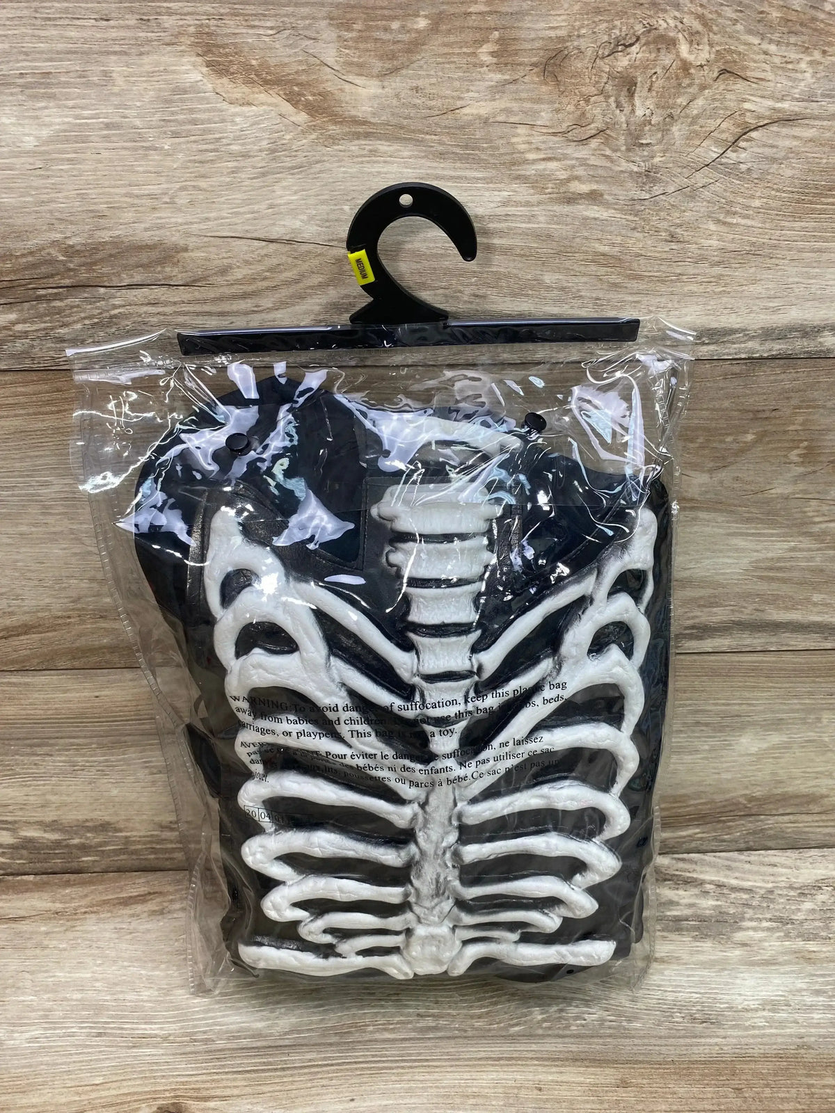 Front view of child’s black Spirit skeleton costume with raised white ribcage, in clear plastic packaging on wood background