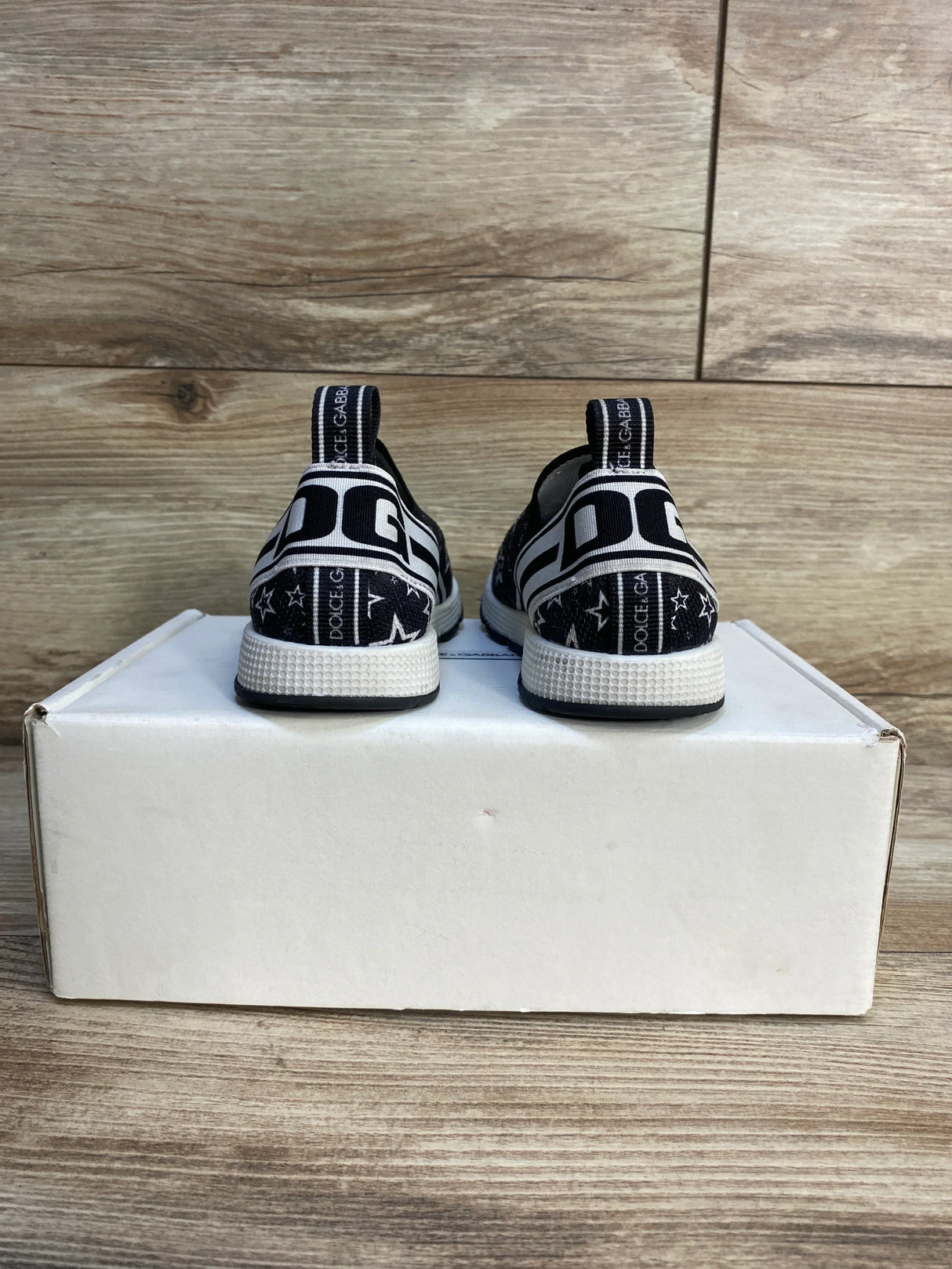 Back view of black toddler sneakers with white soles, star pattern, on a box, wood background