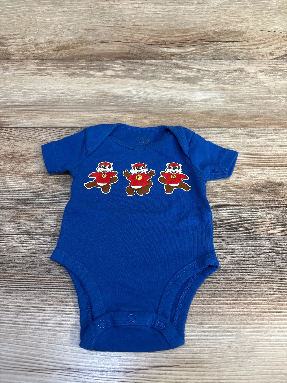Blue baby onesie with three cartoon beavers in red shirts on wood background