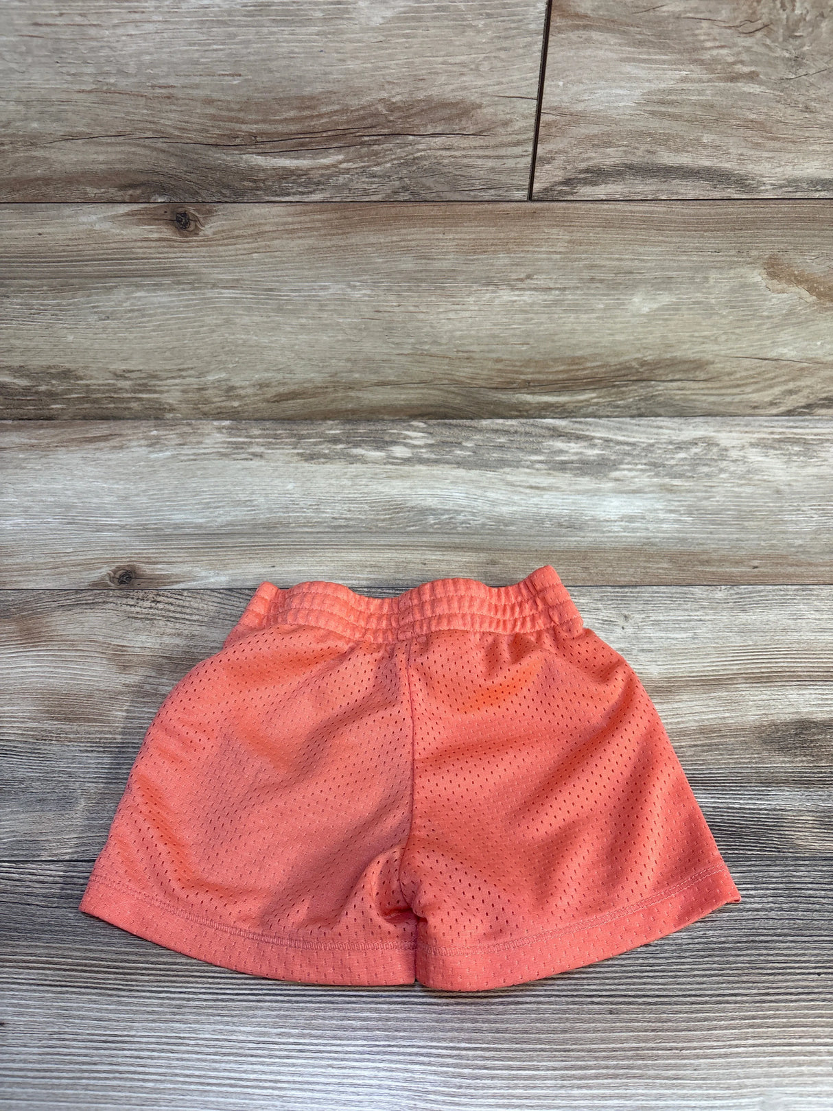Flat lay of Champion coral mesh toddler shorts showcasing elastic pull-on waistband and breathable perforated fabric on wood plank background