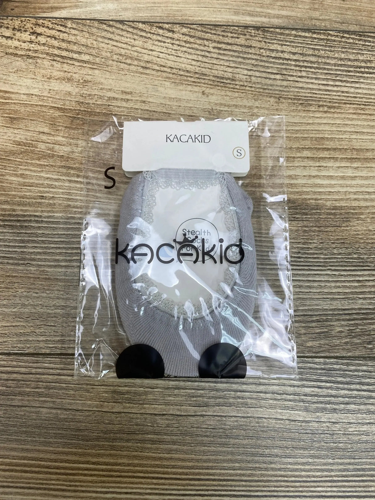 Top-down view of Kacakid Princess Mary Jane baby dress socks in grey with lace trim in clear packaging on light wood background