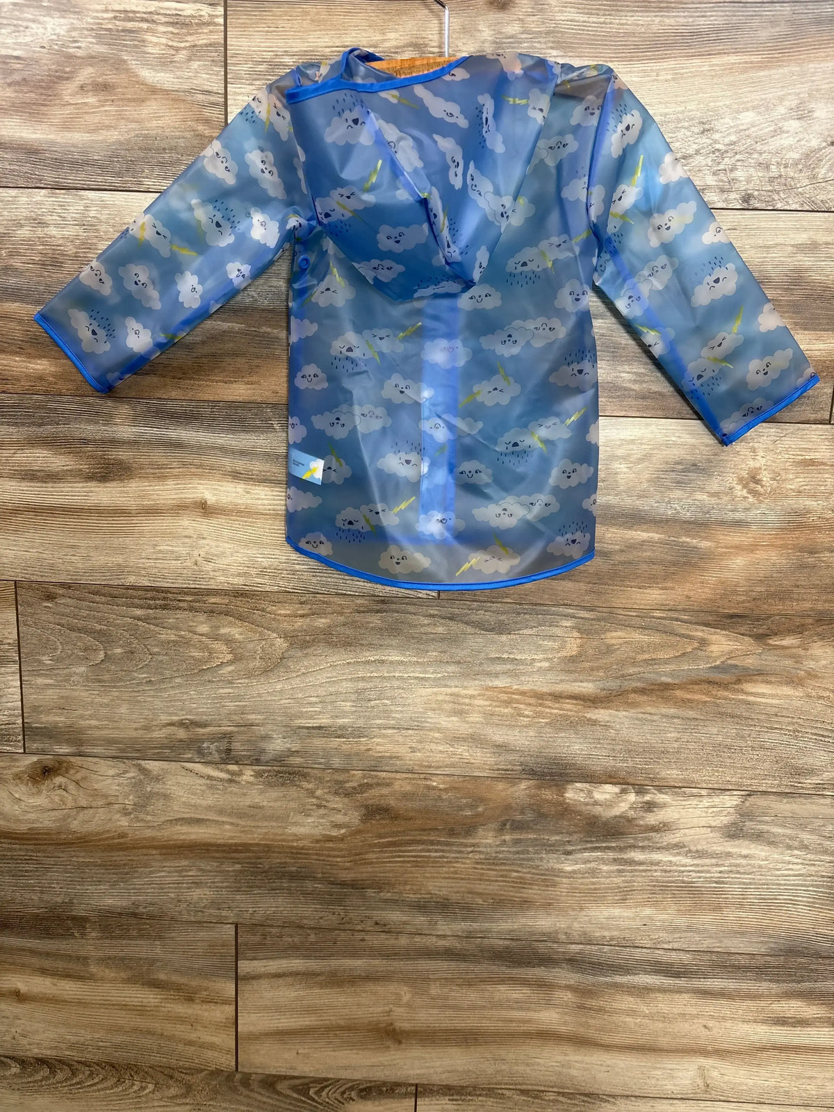 Blue kids raincoat with cloud and lightning print, displayed on wood floor.