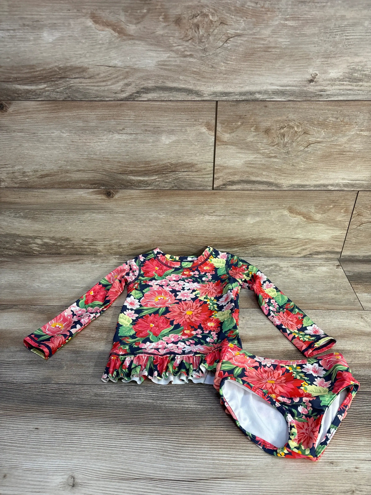 Flat lay of toddler two-piece floral rashguard swimsuit with long-sleeve ruffle-top and matching bottoms on wood background