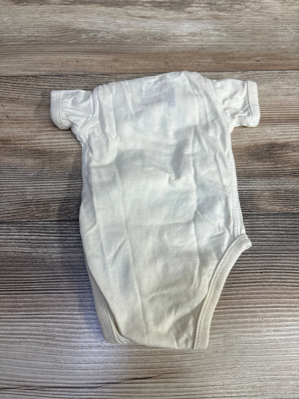 White short-sleeve baby onesie laid flat on wooden surface