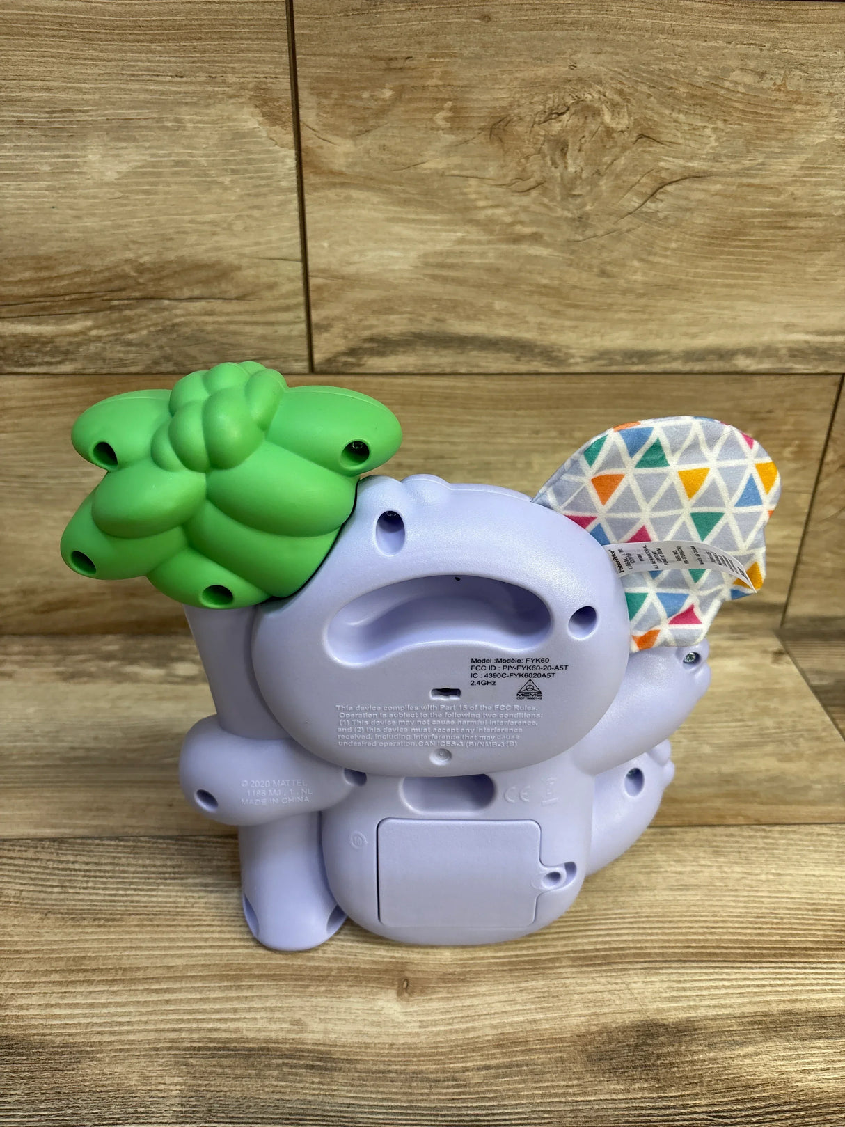 Rear view of Fisher Price Linkimals Counting Koala showing battery compartment, fabric ear, and green topper on wood surface
