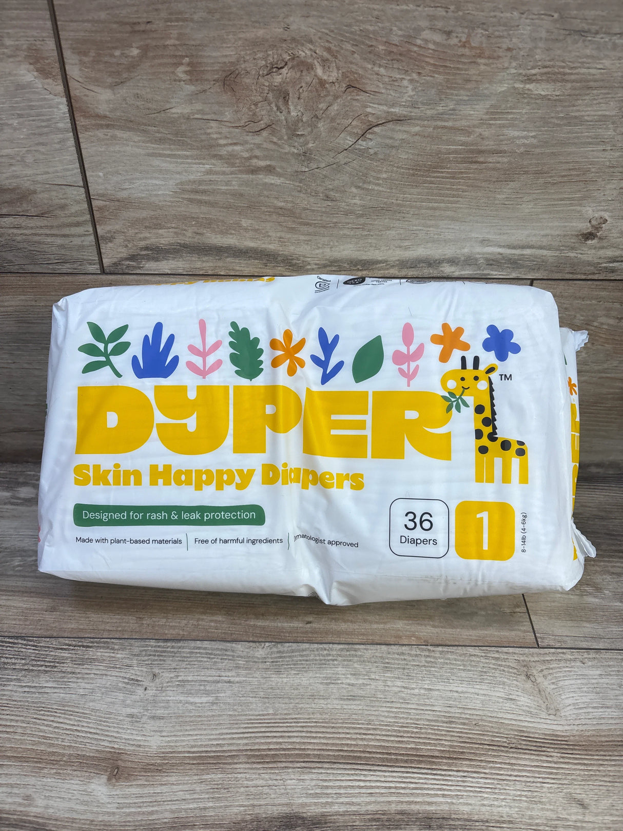 Front view of Dyper Skin Happy Diapers pack Size 1 showing 36 diapers, Skin Happy Diapers text and giraffe on wood floor