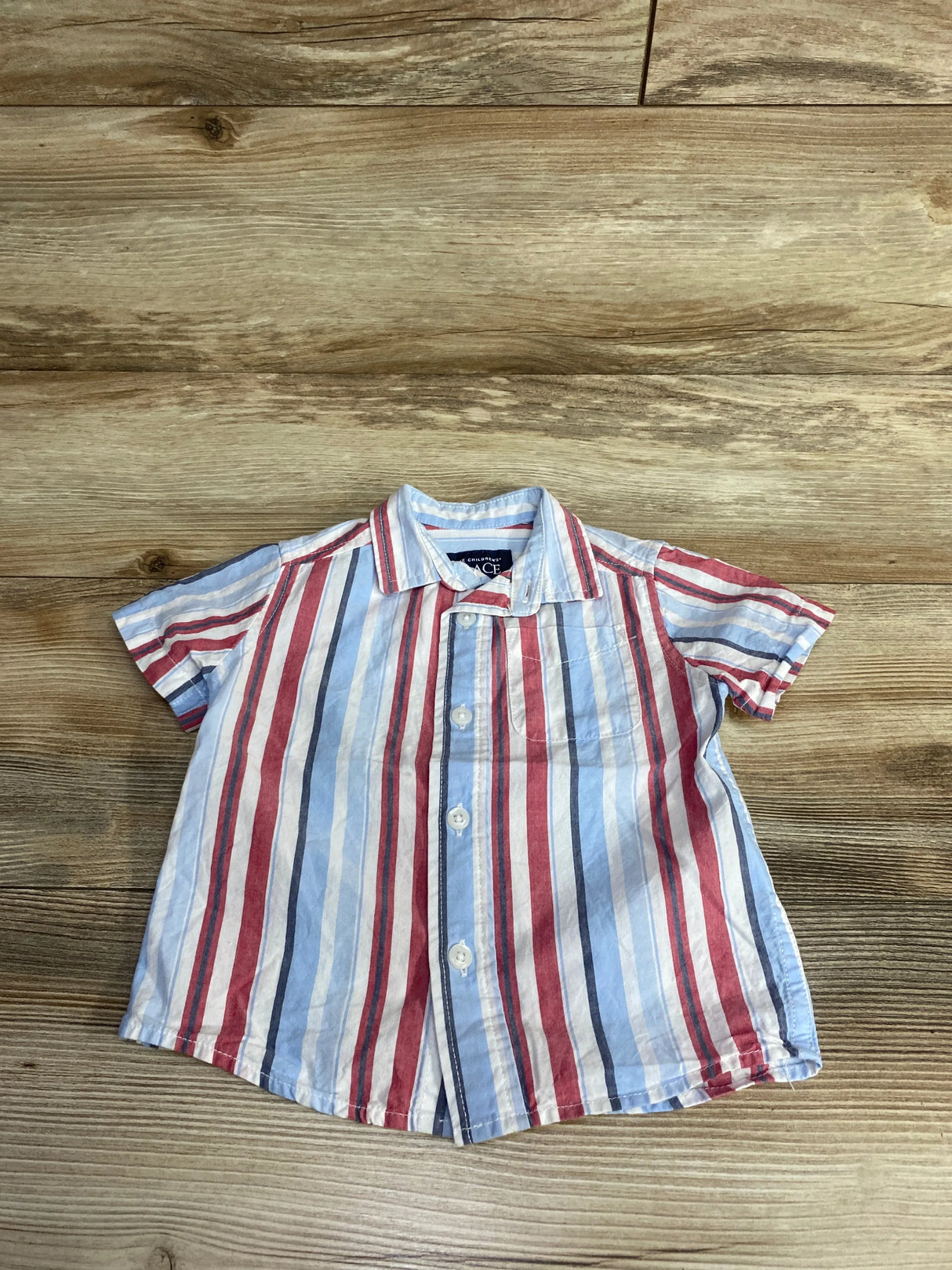 Red white and blue striped short sleeve boys button up shirt on wood background