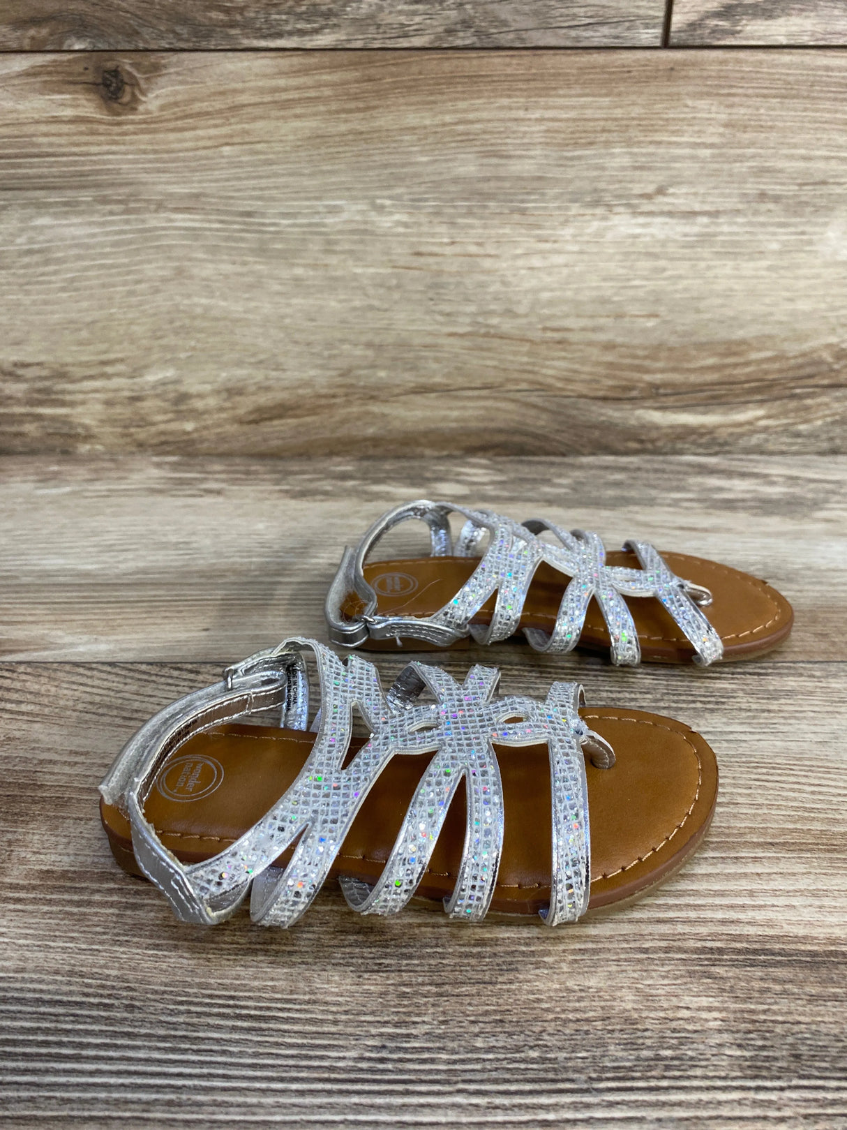 Children's silver glitter strappy sandals on wood background