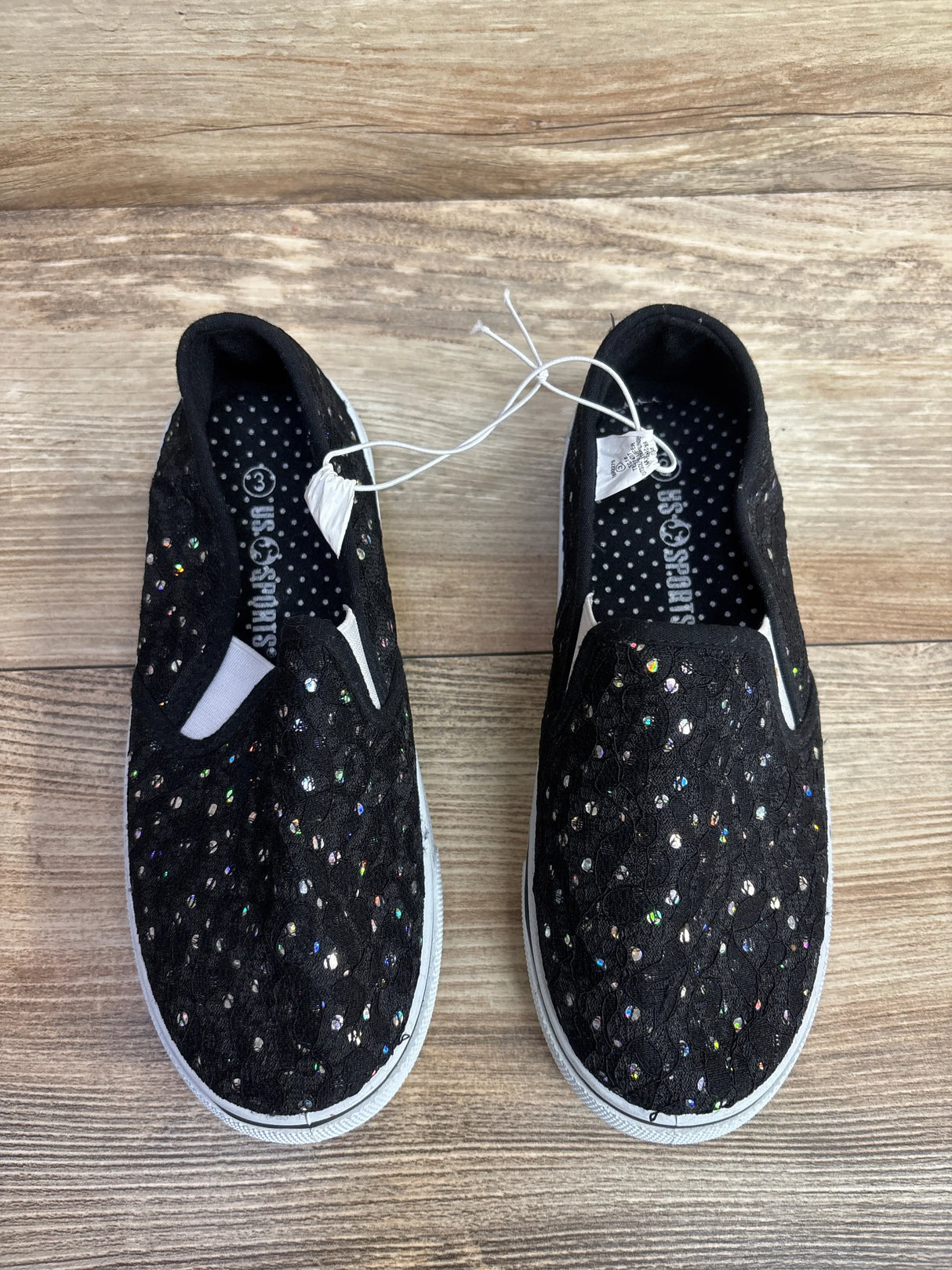Pair of black kids slip-on shoes with glittery sequins on wooden floor, size 3