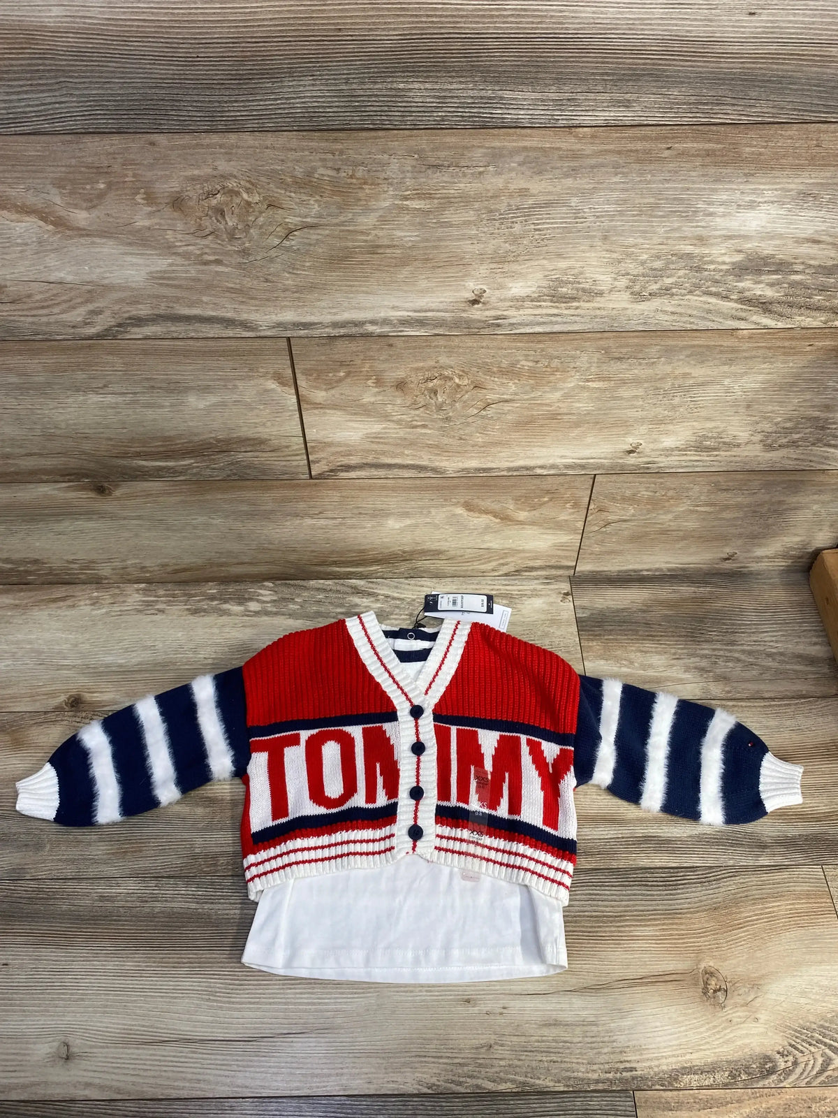 Red and navy striped Tommy Hilfiger baby cardigan with white shirt on wood floor