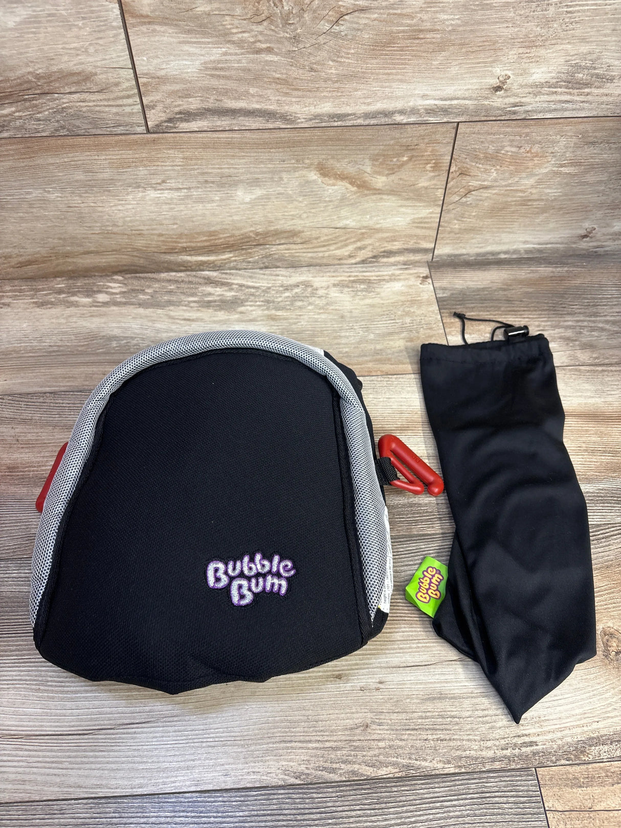 BubbleBum black inflatable booster car seat with grey trim and black storage bag on wood floor