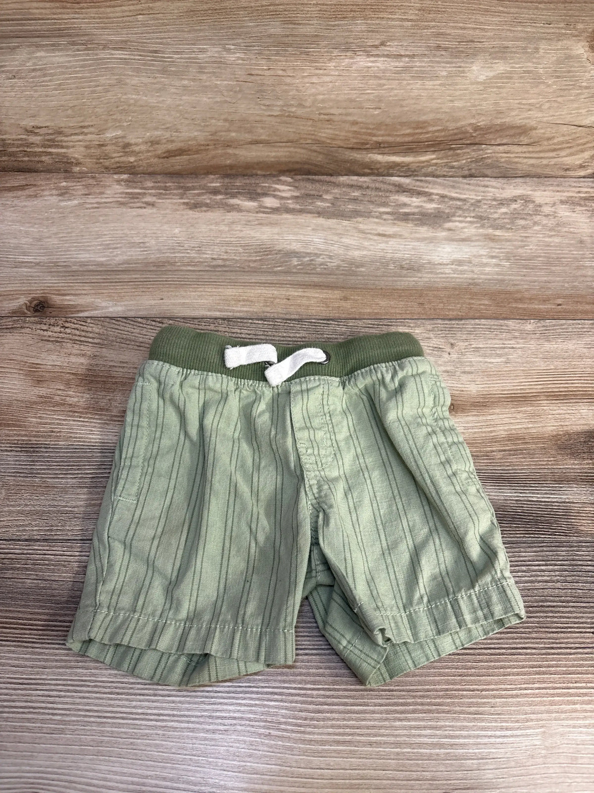 Top-down view of Cat and Jack toddler green striped pull-on shorts with elastic ribbed waistband, white drawstring, and side pockets on wood background