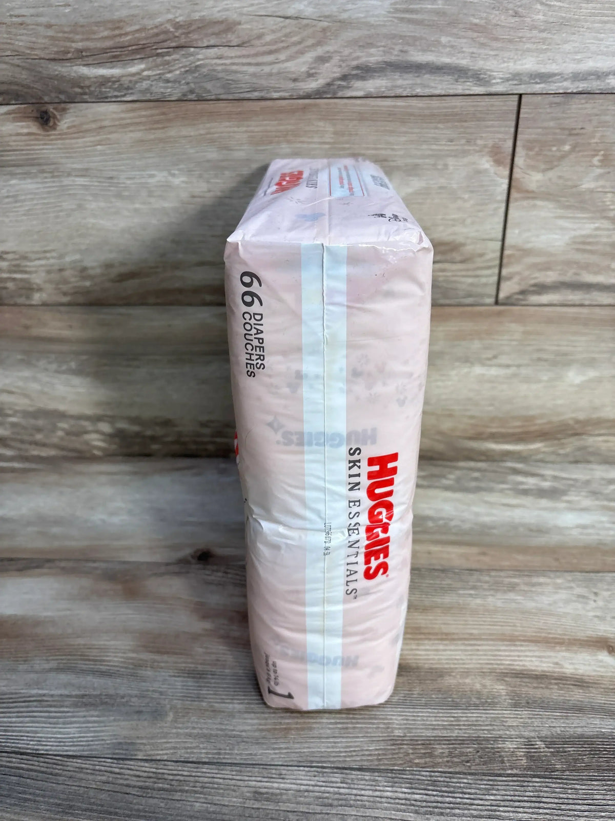 Side view of Huggies Skin Essentials Size 1 diaper pack showcasing 66-count label and red Huggies logo on wood floor