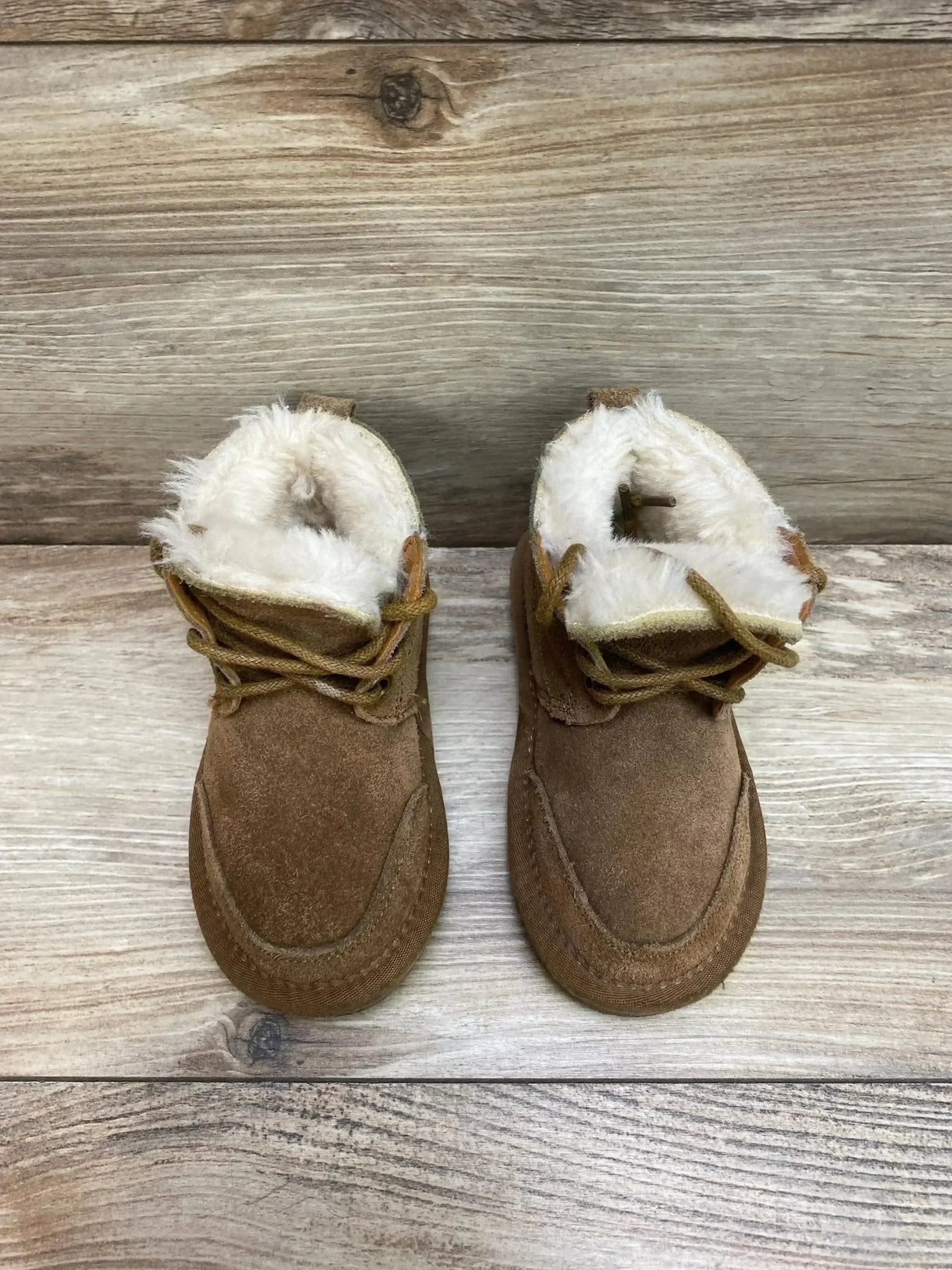Top-down view of toddler chestnut Lamo chukka suede boots showing faux fur lining and lace ties on wood background