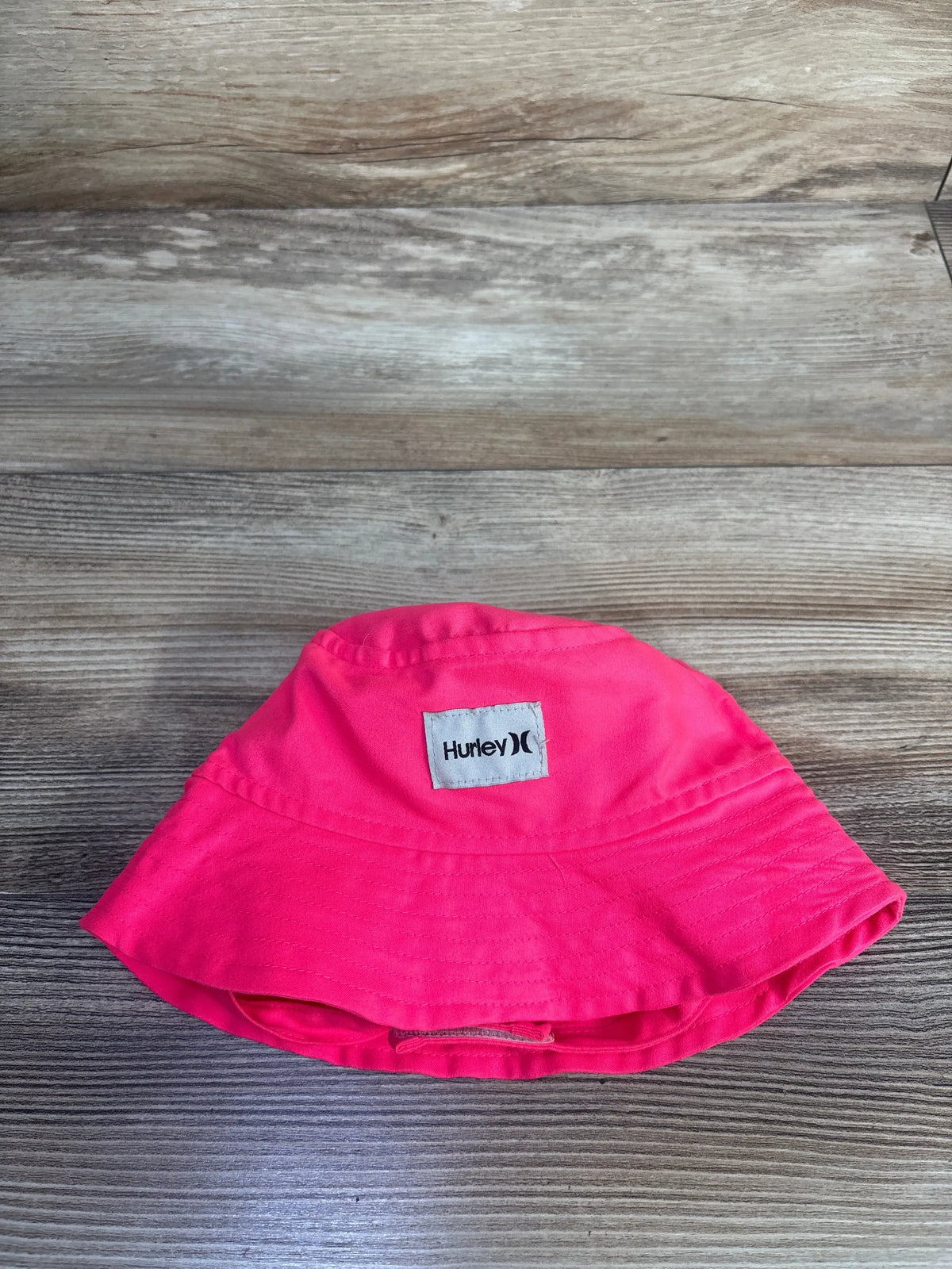 Front view of pink Hurley bucket hat, size 18m, showcasing stitched brim and chin strap on a wood-grain background