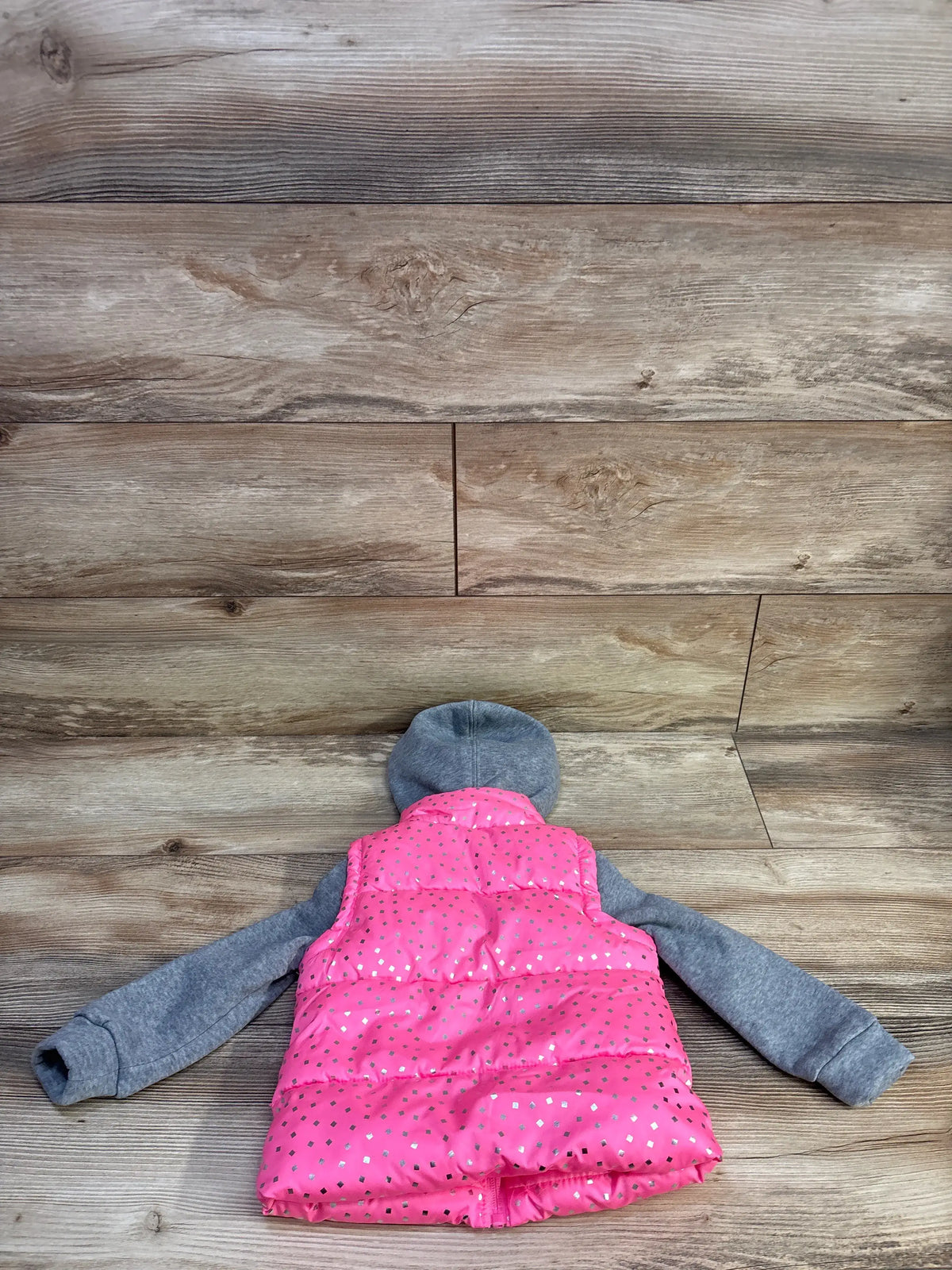 Back view of pink 2fer puffer jacket showing quilted vest with silver foil dots and attached gray hoodie sleeves on wood