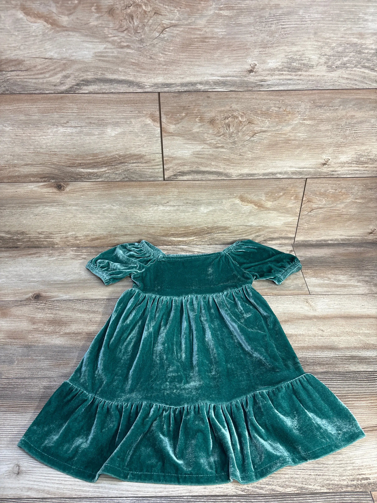 Front view of Carter’s green velvet dress in size 4T showcasing short puff sleeves and ruffled hem on a wood-look background