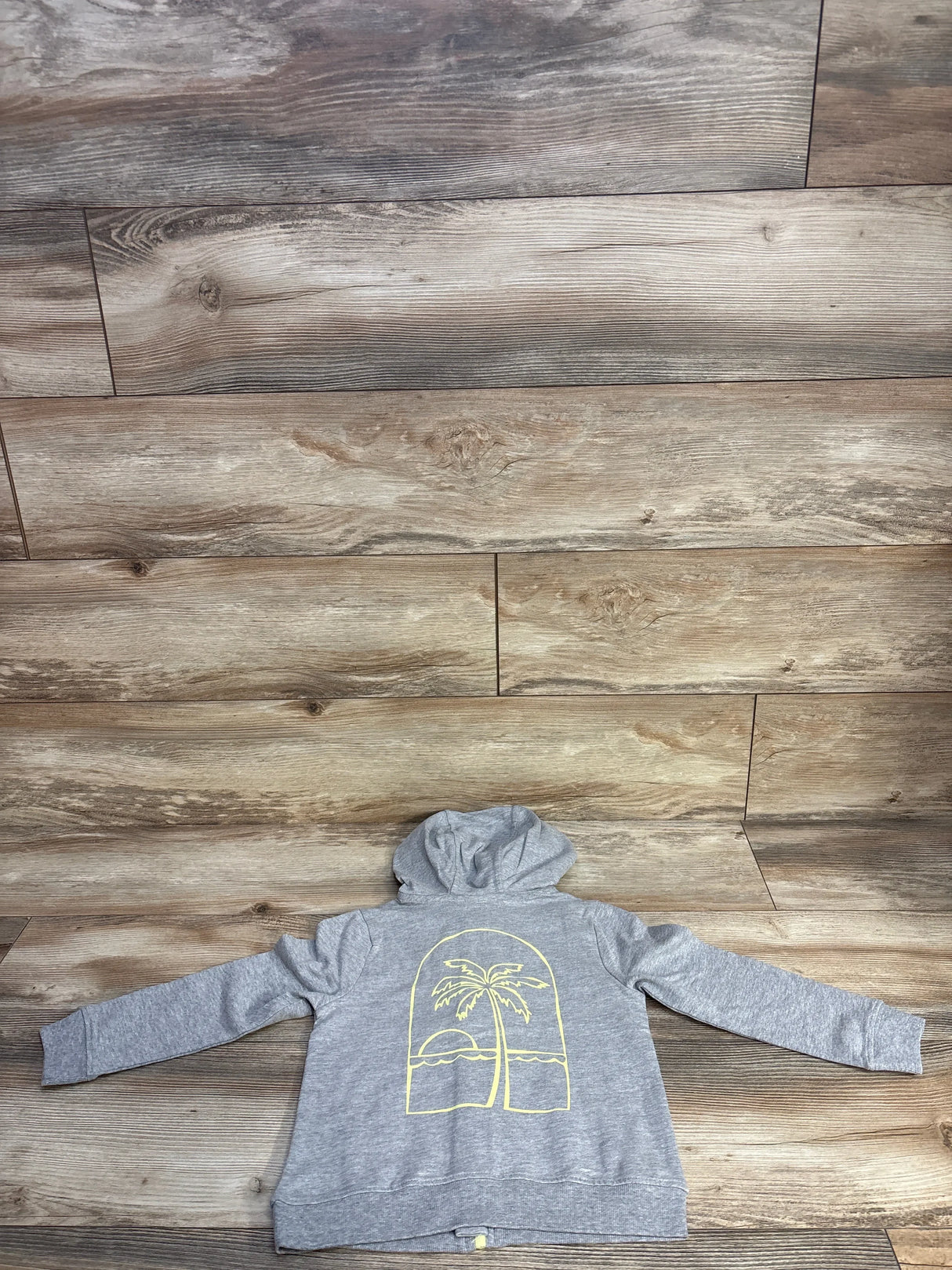 Gray hoodie with yellow palm tree and sunset graphic on wooden background