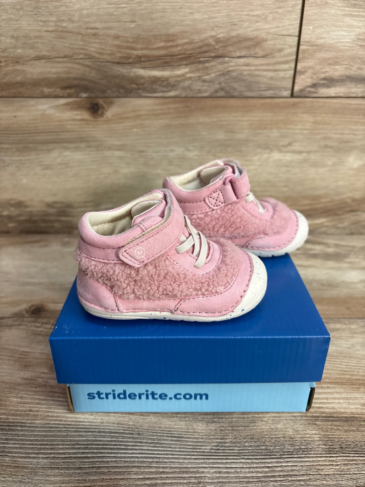 Pink toddler shoes with fleece texture on a blue Striderite shoebox on wooden floor