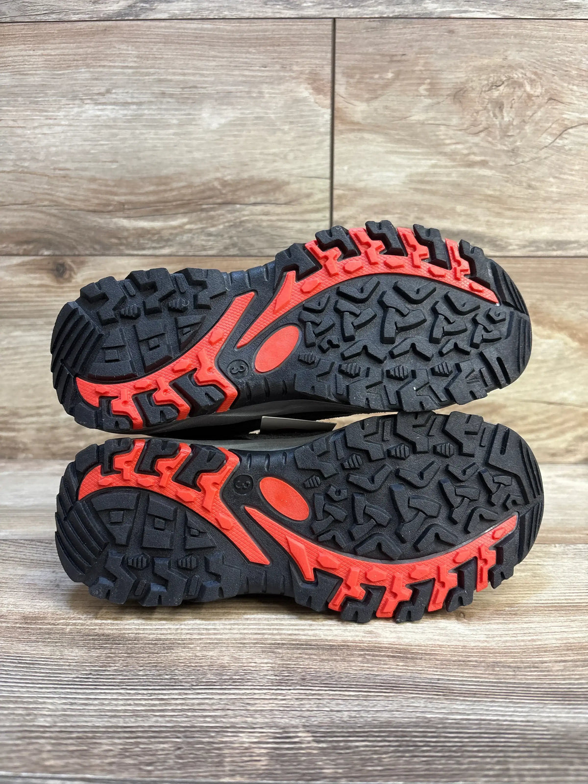 Sole view of Cat and Jack Patsy hiking boots showcasing black and red rugged lug tread on wood plank floor