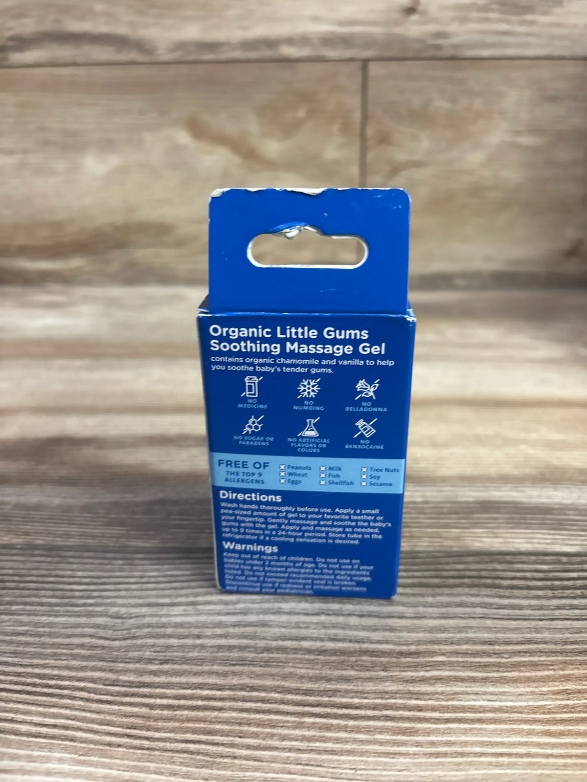 Back view of Mommy’s Bliss Organic Little Gums Soothing Massage Gel package showing directions and allergen information on wood background