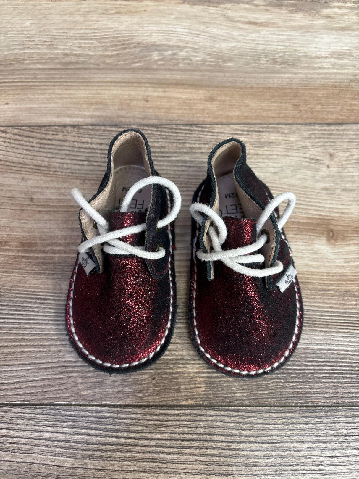 Pair of glittery dark red toddler shoes with white laces on wooden floor