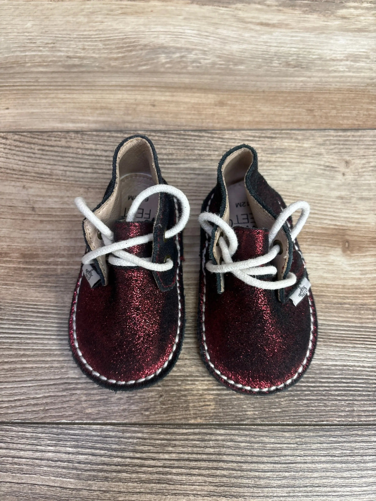 Pair of glittery dark red toddler shoes with white laces on wooden floor