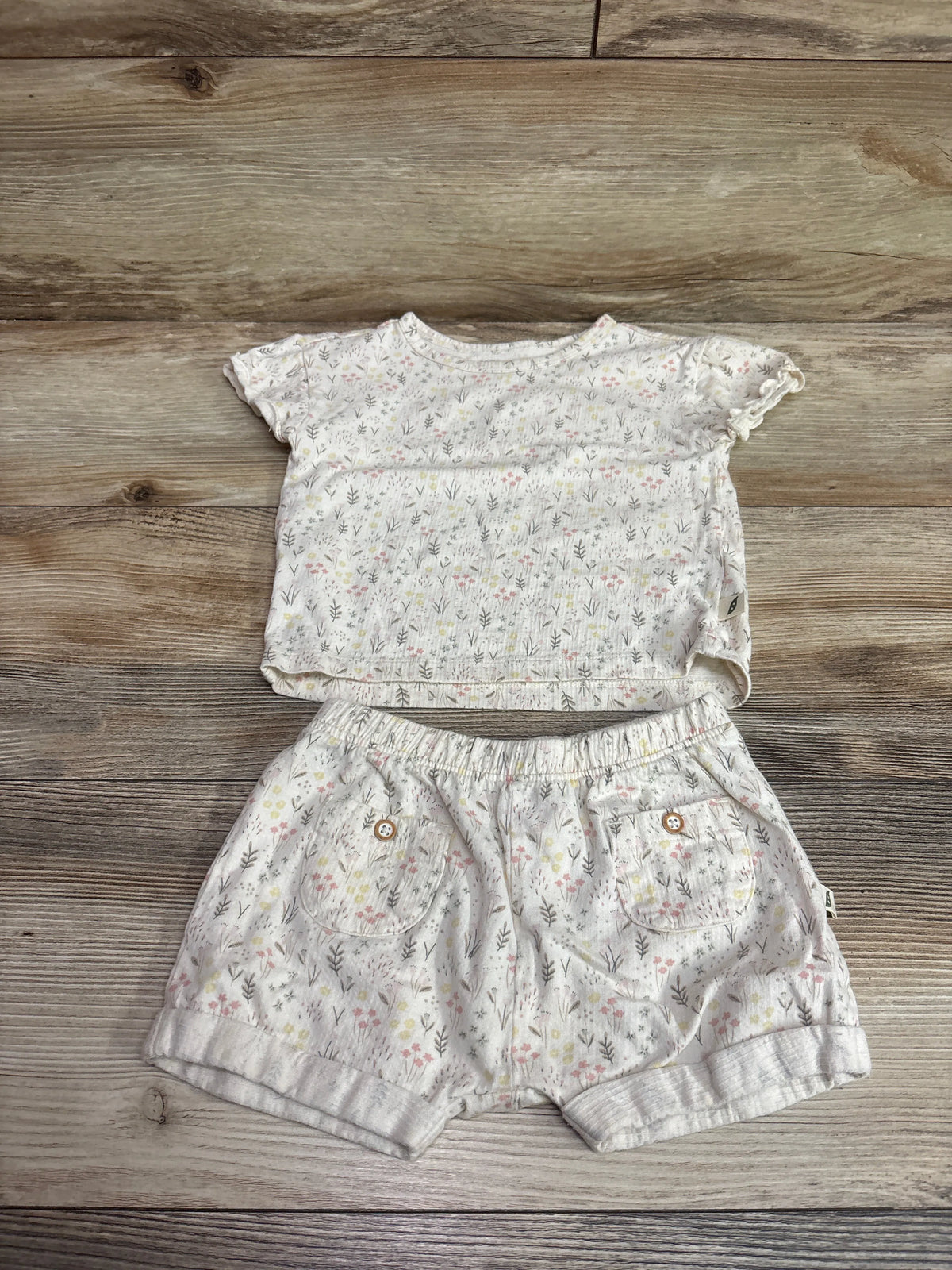 Top-down view of ivory Easy Peasy shirt and shorts set showcasing floral print, pockets, and elastic waist on wood