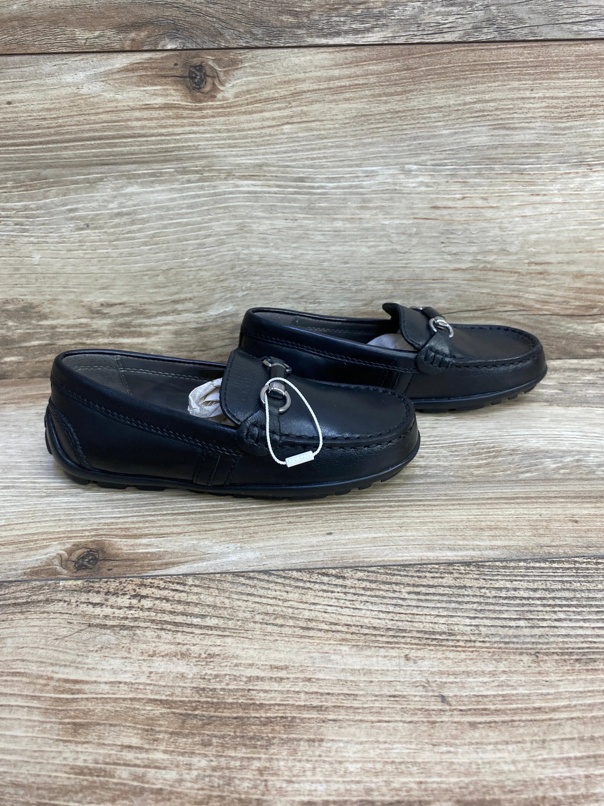 Side view of toddler Geox black chain loafers (size 10C) showing silver chain detail and stitched moc toe on wood background