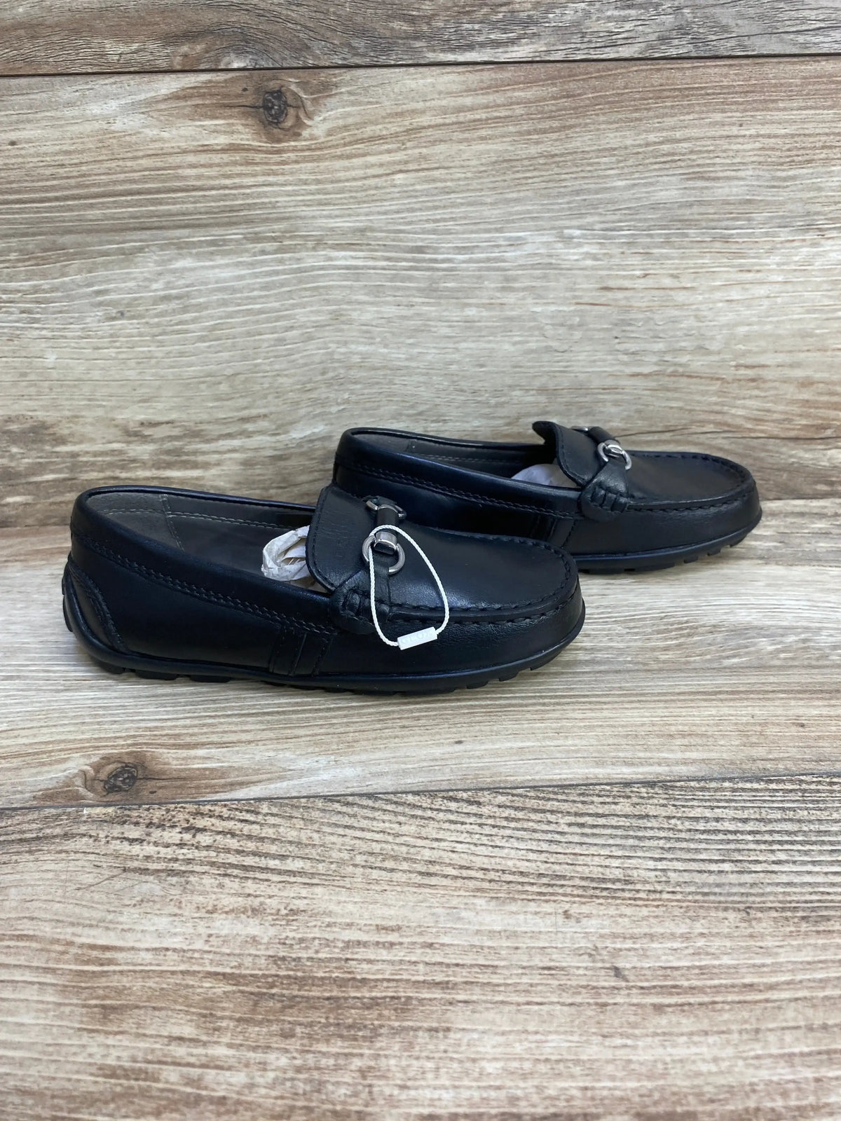 Side view of toddler Geox black chain loafers (size 10C) showing silver chain detail and stitched moc toe on wood background